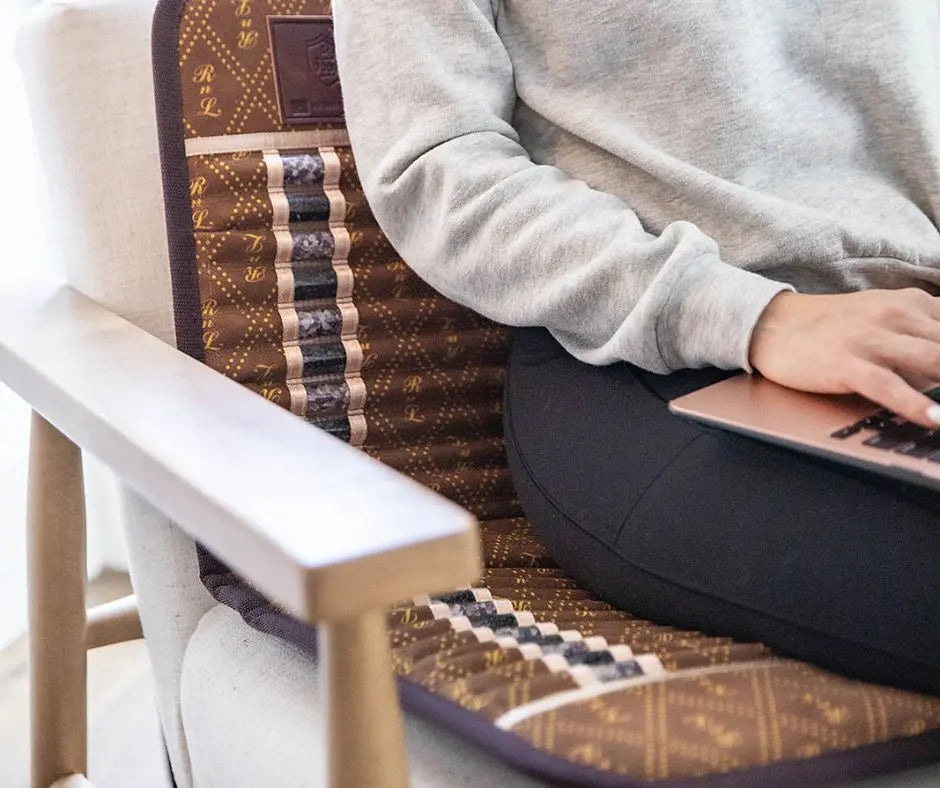 Person sitting on a chair using a brown far infrared mat while typing on a laptop
