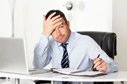 Stressed businessman holding his head at an office desk with laptop and paperwork