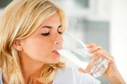 Close-up of a woman drinking a glass of clear water, header image for an article about alkaline water