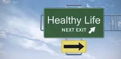 Green highway sign reading ‘Healthy Life NEXT EXIT’ with a yellow directional arrow against a blue sky