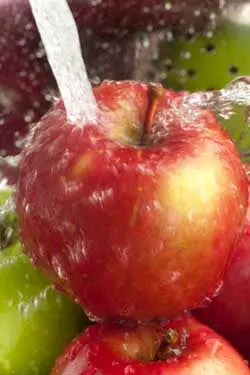 Close-up of red apples being rinsed under a stream of water to remove pesticide residue