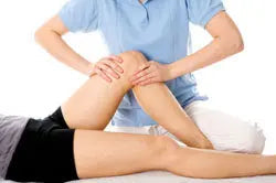 Physiotherapist performing knee mobilization on a patient’s leg on a treatment table in a clinic