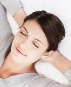 Woman lying on a pillow with eyes closed, calmly resting in a bright, soft setting