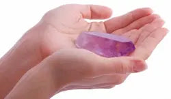 Hands holding a small polished purple amethyst crystal in open palms against a white background