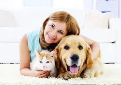 Woman smiling with a golden retriever and an orange and white cat on a living room rug