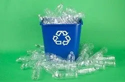 Blue recycling bin with white recycling symbol filled with clear plastic bottles and scattered bottles on green background