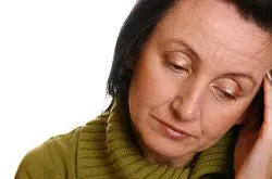 Middle-aged woman in a green sweater holding her head and looking fatigued against a white background