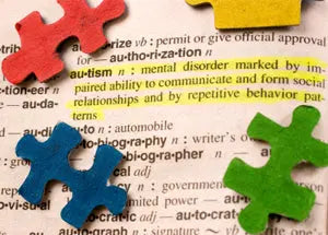 Close-up of colored jigsaw puzzle pieces on a dictionary page with the word ‘autism’ highlighted in yellow