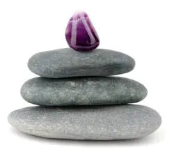 Three stacked gray stones with a small purple crystal on top, symbolizing balance and energy healing