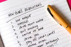 Notebook page titled New Year’s Resolutions with a handwritten list of goals and a gold pen on a pink background
