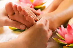 Therapist’s hands massaging a person’s foot during a reflexology session with pink lotus flowers in the background