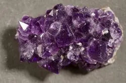 Close-up of an amethyst cluster showcasing deep purple crystalline points and druzy texture on a gray surface