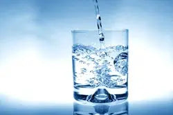 Glass of water being poured with visible bubbles against a soft blue background