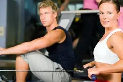 Two people using rowing machines in a gym during a cardio workout illustrating weight loss