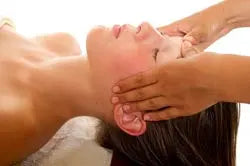Woman lying with eyes closed receiving a relaxing scalp massage in a spa setting