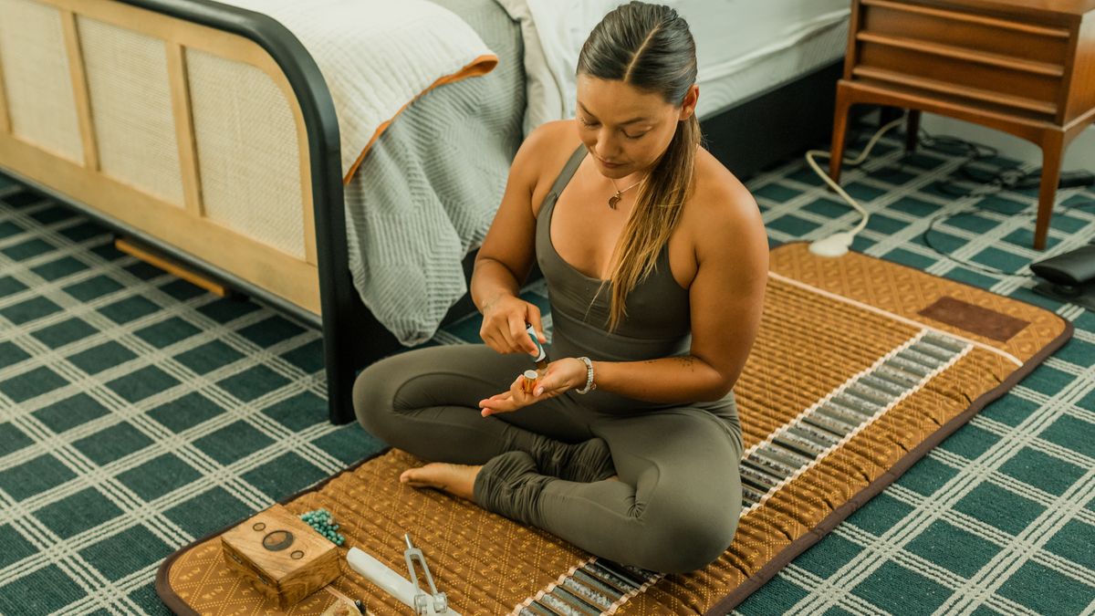 Woman seated cross-legged on a BioMat using a small bottle in a bedroom