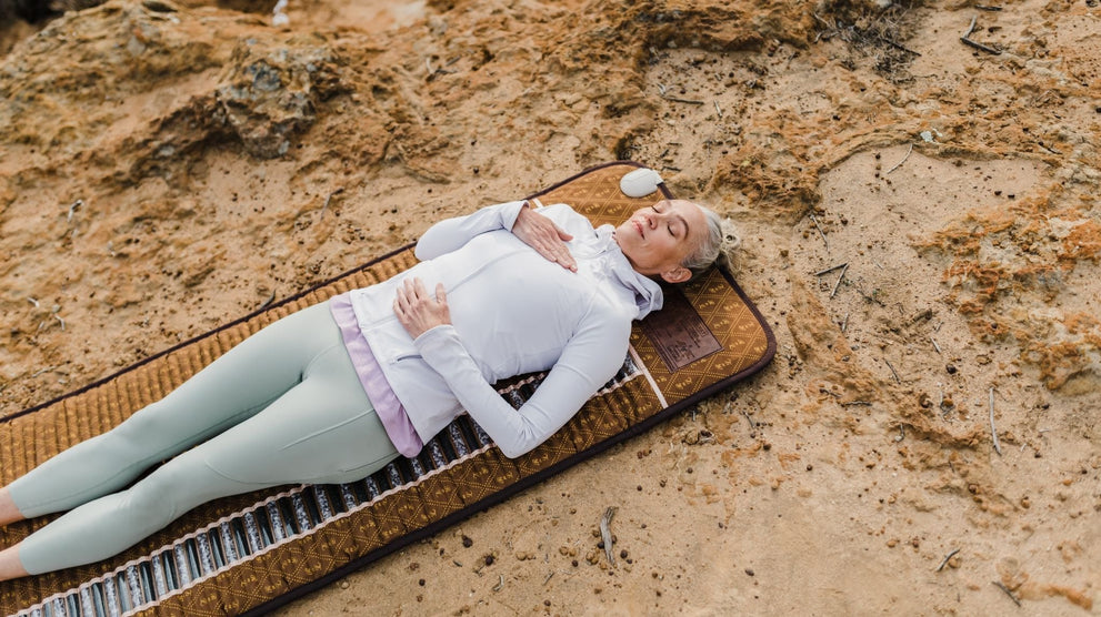 Woman relaxing on a BioMat infrared mat outdoors on sandy ground